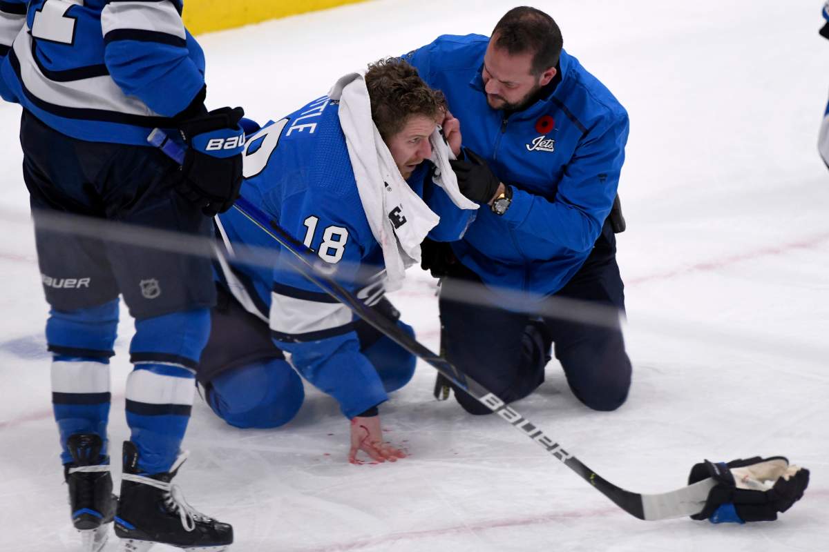Winnipeg Jets’ Bryan Little (18) is helped after getting hit in the head with the puck against the New Jersey Devils during third period NHL action in Winnipeg on Tuesday, Nov. 5, 2019.