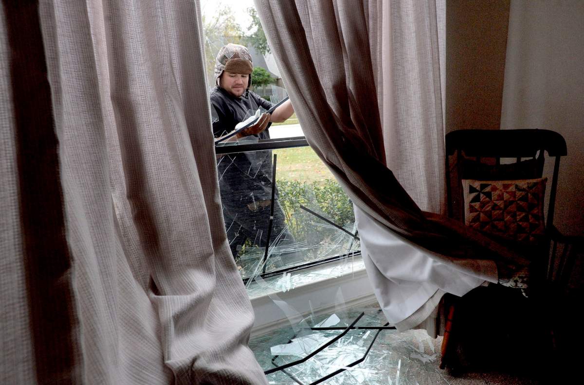Adrian Torres pulls shards of glass from a window frame following an explosion at the TPC plant Wednesday, Nov. 27, 2019, in Port Neches, Texas. (Kim Brent/The Beaumont Enterprise via AP)