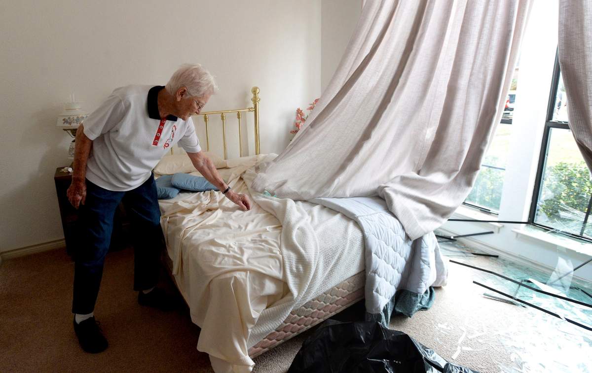 Wilma Shahan picks at shards of glass littering the bed after an explosion at the TPC plant shattered the window, Wednesday, Nov. 27, 2019, in Port Neches, Texas. (Kim Brent/The Beaumont Enterprise via AP)