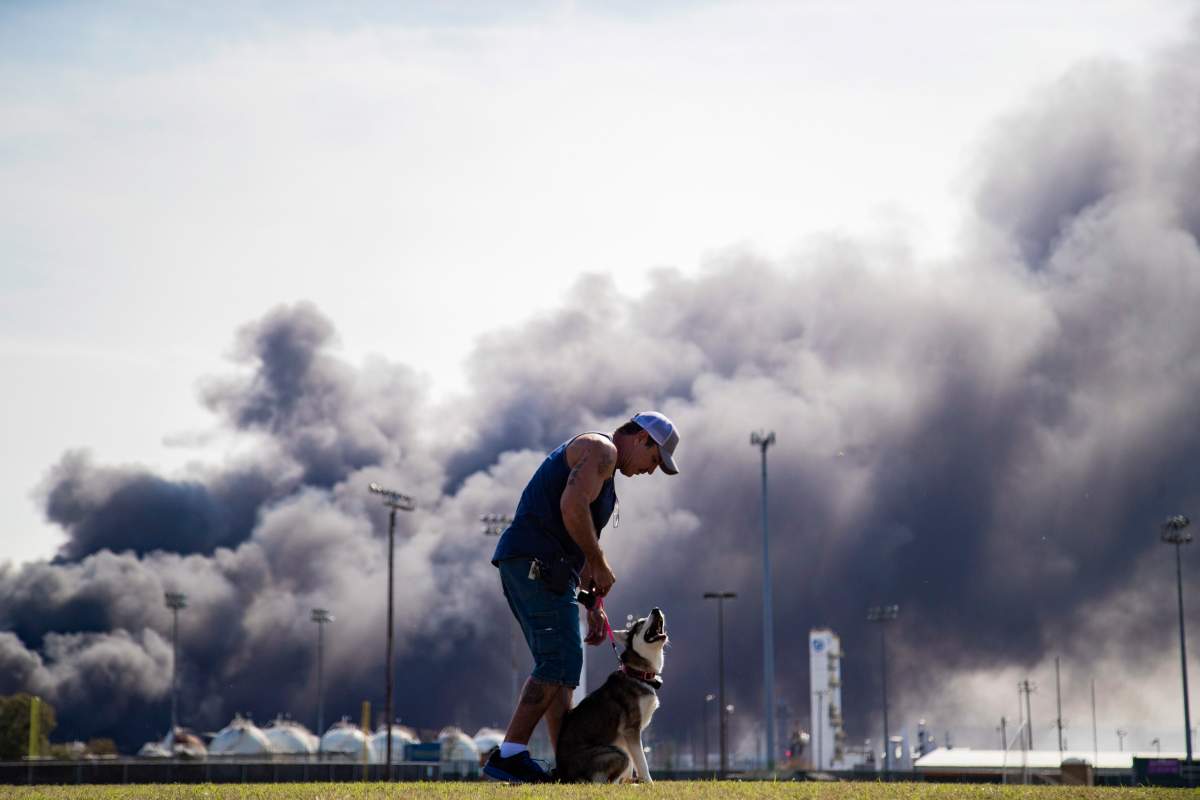 Ray Moore trains his dog Aries with a cloud of smoke in the background from the TPC Group Port Neches Operations explosion. (Marie D. De Jesús/Houston Chronicle via AP)