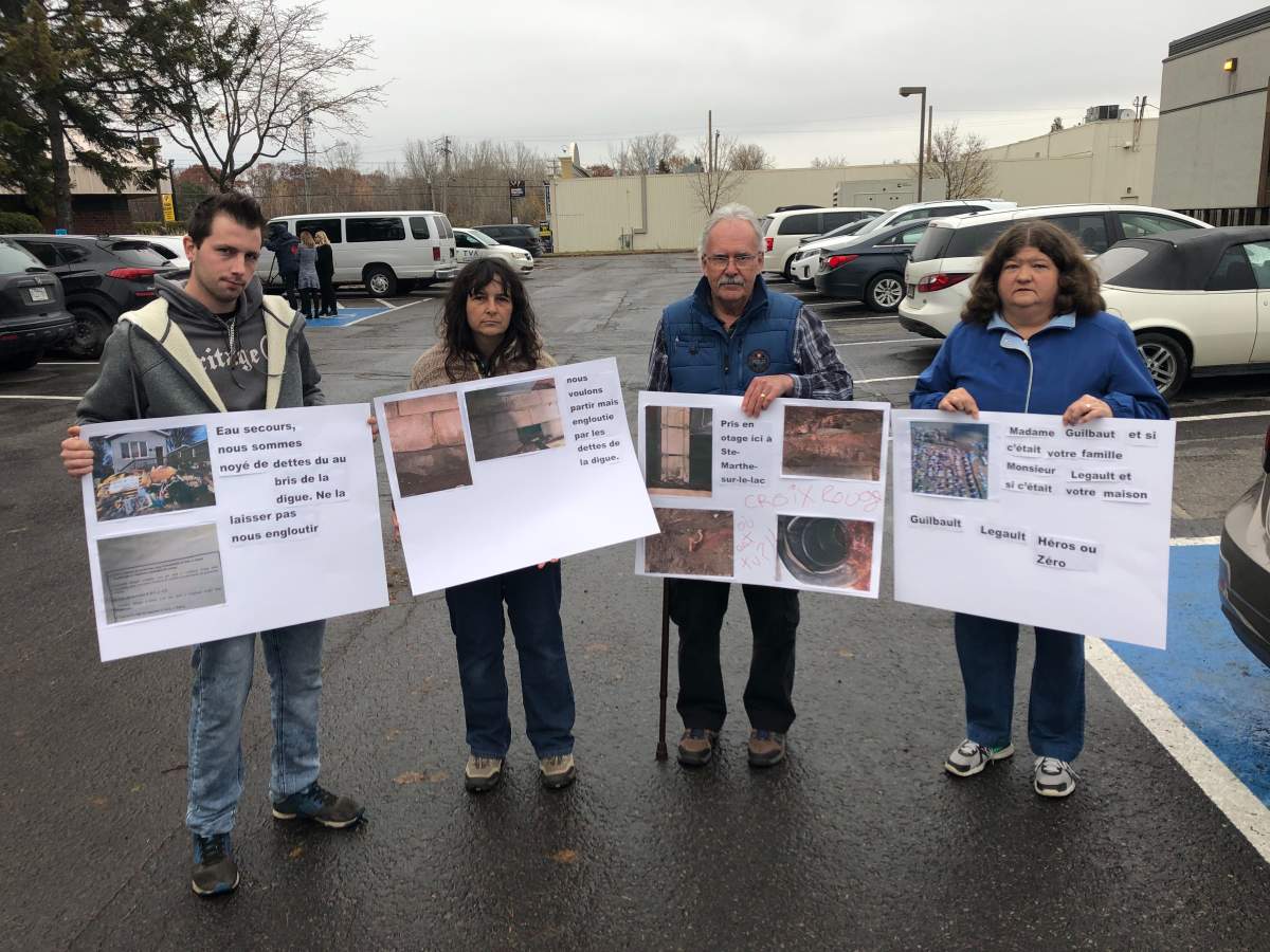 Sainte-Marthe-sur-le-Lac residents hold posters showing pictures of the flood damage to their homes outside the press conference on Monday.