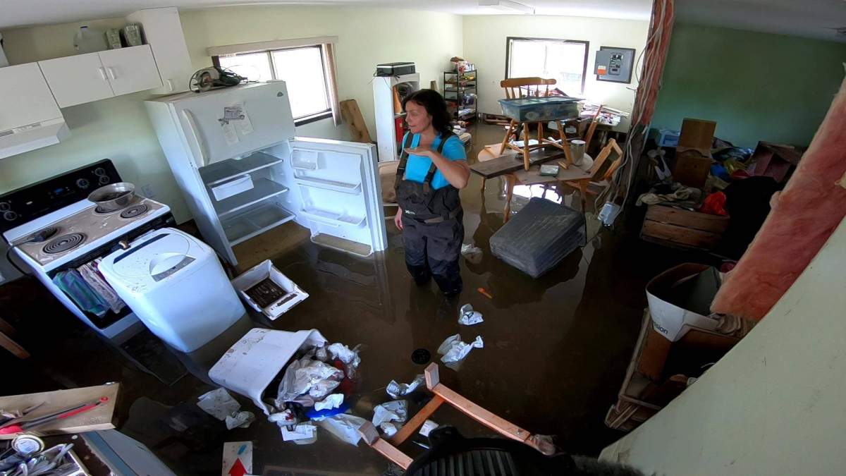 Jennifer Houghton stands in her flooded home indicating the high water mark with her hand in May 2018.