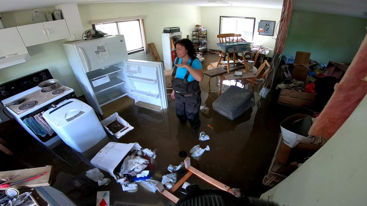 Jennifer Houghton stands in her flooded home indicating the high water mark with her hand in May 2018. 