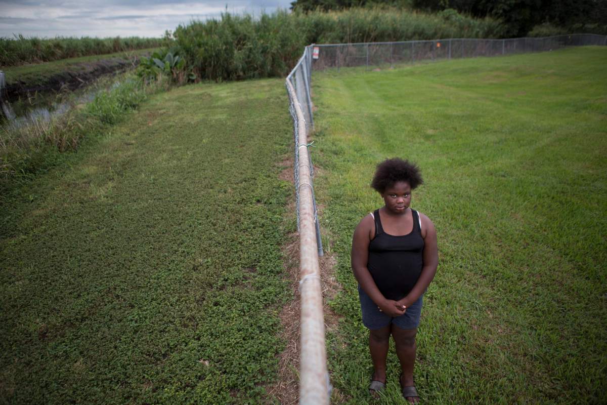 In this Nov. 4, 2019 photo, Kaniyah Patterson stands in front of a sugar cane field behind her home in Pahokee, Fla. Patterson says that smoke from sugar cane burns trigger her asthma.