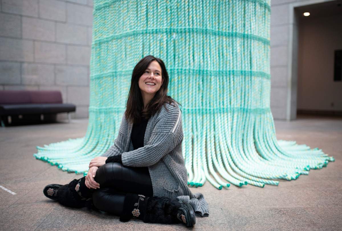 Rachelle Dickenson, one of the curators of Àbadakone, an exhibit of contemporary Indigenous art, sits in front of Aka, a work by the Mata Aho Collective, at the National Gallery of Canada in Ottawa, on Friday, Dec. 6, 2019. The column, which is made of marine rope, was made by four women artists using a customary Maori twining technique, and was eventually finished on site at the gallery.