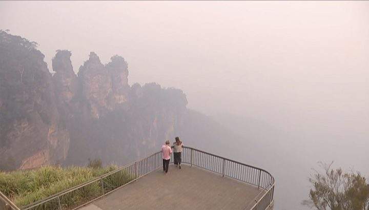In this image made from video, two people watch from a look out of smoke from wildfire, Monday, Dec. 23, 2019, in the Blue Mountains, New South Wales, Australia.