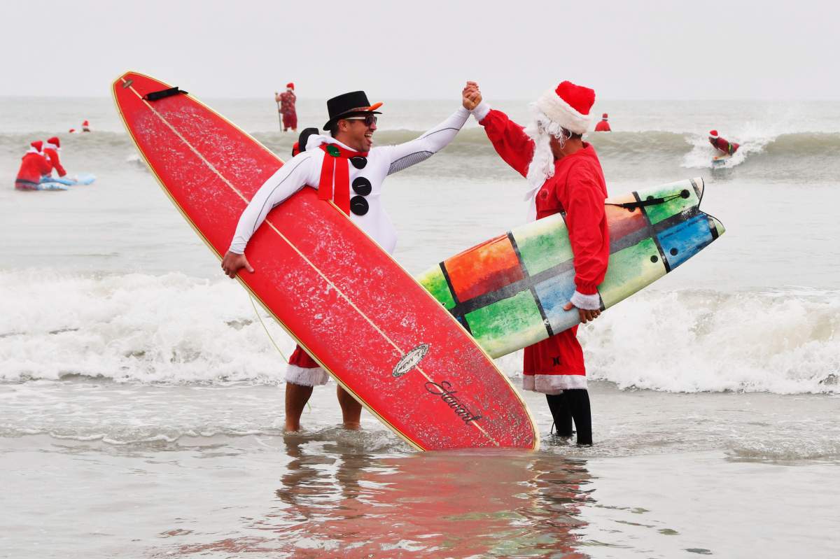 George Trosset Jr. and George Trosset, who started surfing in Santa and Christmas costumes ten years ago behind their house on Christmas Eve, high five each other during the 10th annual Surfing Santas event in Cocoa Beach, Fla., Dec. 24, 2019.