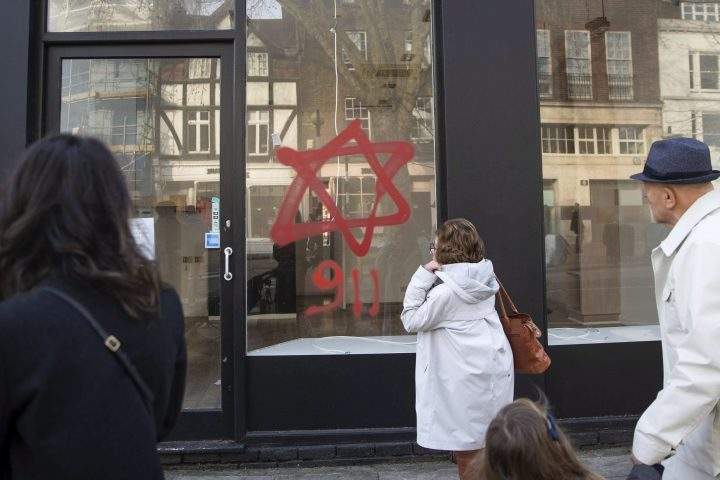 People look at anti-Semitic graffiti on a shop window in Belsize Park, North London, Sunday, Dec. 29, 2019. A synagogue and several shops in north London have been daubed with anti-Semitic graffiti during the Jewish festival of Hanukkah.