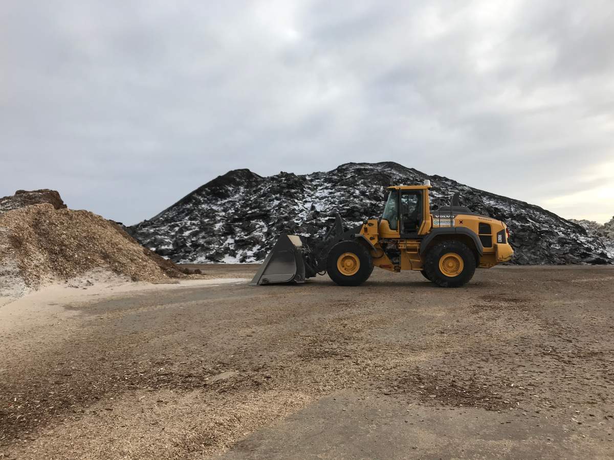 A huge pile of shingles waiting to be turned to asphalt sits behind an idle front end loader.