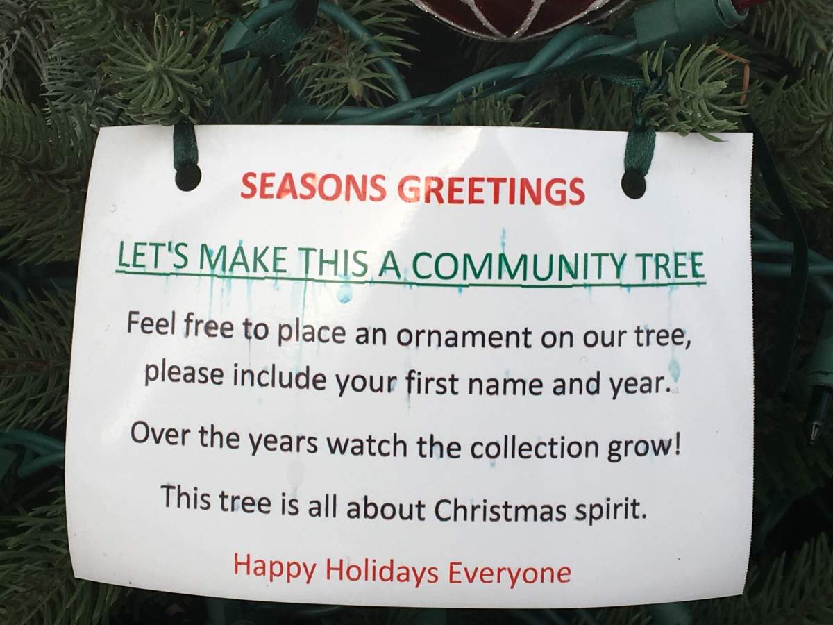 Sign on community tree urging neighbours to join in the holiday spirit.