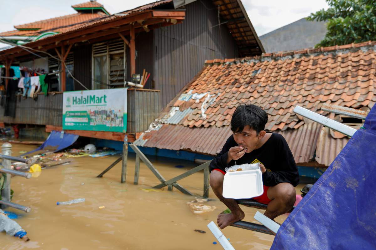 Muhamad Fathur Rizki, 19, eats his lunch outside his house, flooded after heavy rains in Jakarta, Indonesia, January 2, 2020. REUTERS/Willy Kurniawan