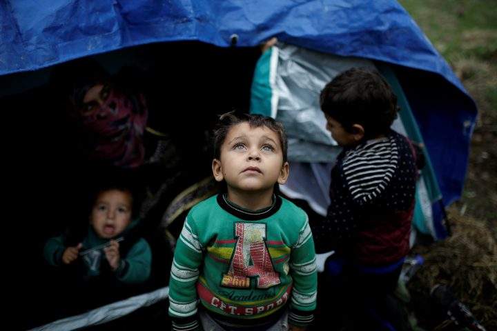 A Syrian refugee boy stands in front of his family tent at a makeshift camp for refugees and migrants next to the Moria camp on the island of Lesbos, Greece, Nov. 30, 2017. 