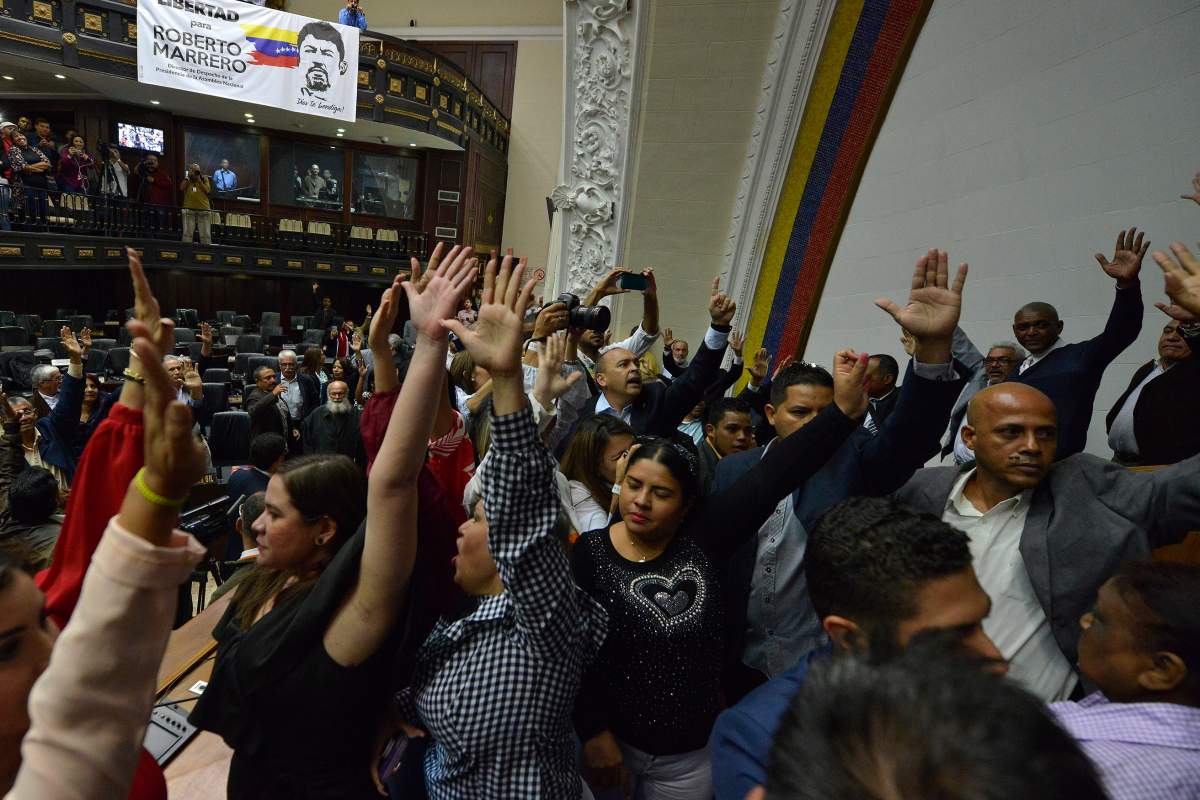 Lawmakers raise their hands to vote in lawmaker Luis Parra as president of the National Assembly, while many opposition lawmakers, including Assembly President Juan Guaido are blocked by police from entering the session, in Caracas, Venezuela, Sunday, Jan. 5, 2020.