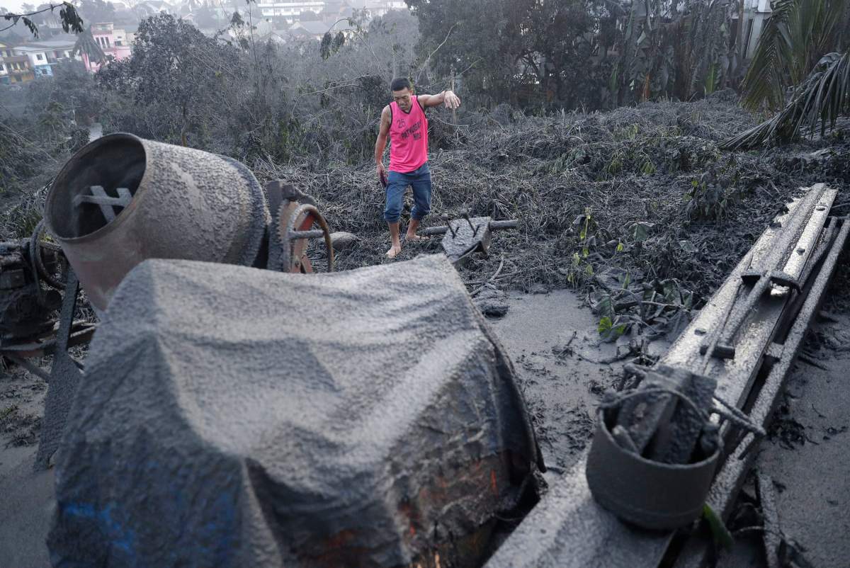 A man walks along ash fall covered plants and equipment as Taal Volcano continues to spew ash on Monday Jan. 13, 2020, in Tagaytay, Cavite province, south of Manila, Philippines.