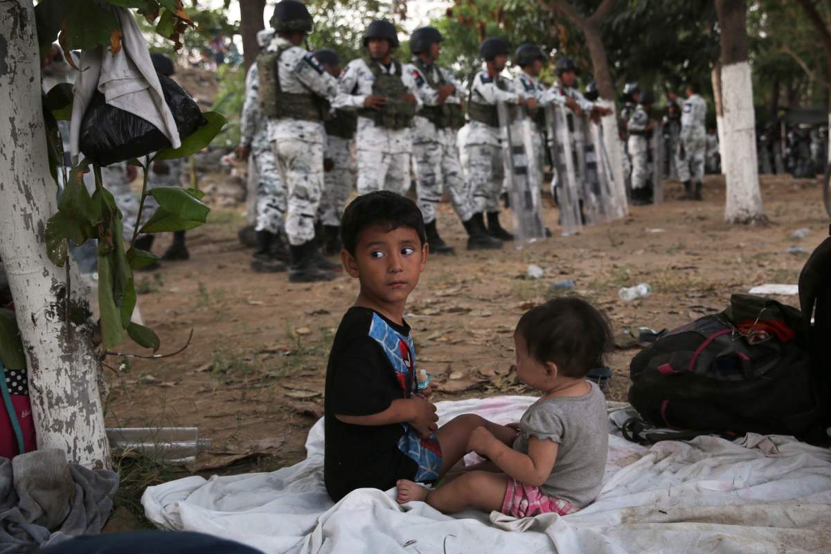 With a line of Mexican National Guardsmen behind them, a couple of migrant children campout on the Mexican shore of the Suchiate river on the border with Guatemala, near Ciudad Hidalgo, Mexico, Monday, Jan. 20, 2020.