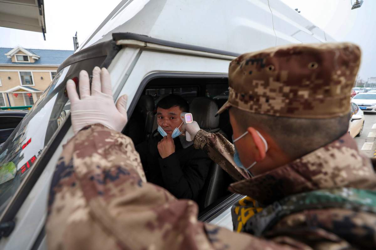 A militia member uses a digital thermometer to take a driver’s temperature at a checkpoint at a highway toll gate in Wuhan in central China’s Hubei Province, Thursday, Jan. 23, 2020.