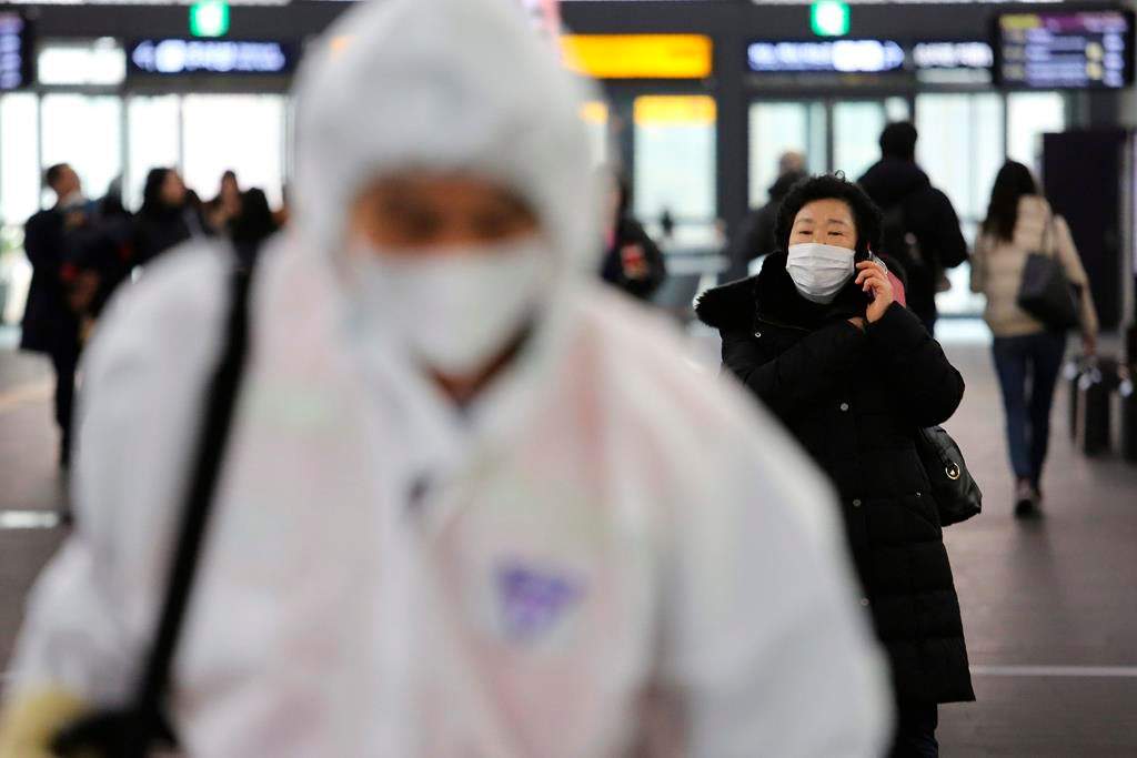 A woman wears a mask as an employee works to prevent a new coronavirus at Suseo Station in Seoul, South Korea, Friday, Jan. 24, 2020.