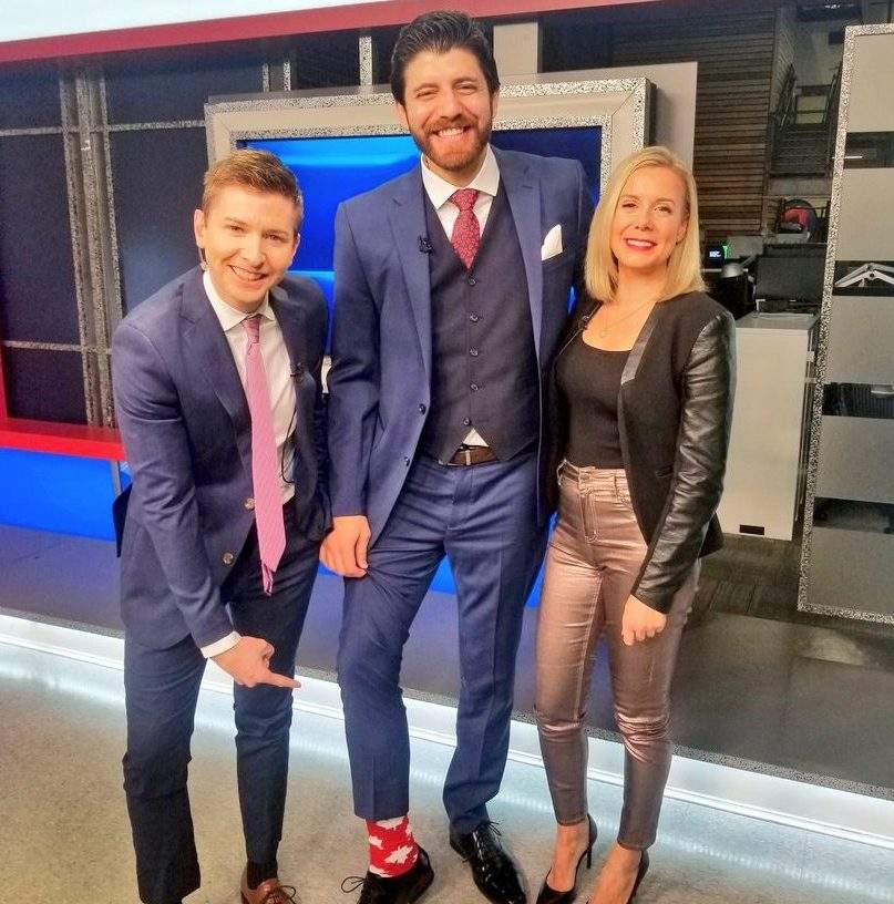 Global News Morning’s Paul Brothers points to Tareq Hadhad’s maple leaf sock as they pose with co-host Alyse Hand.