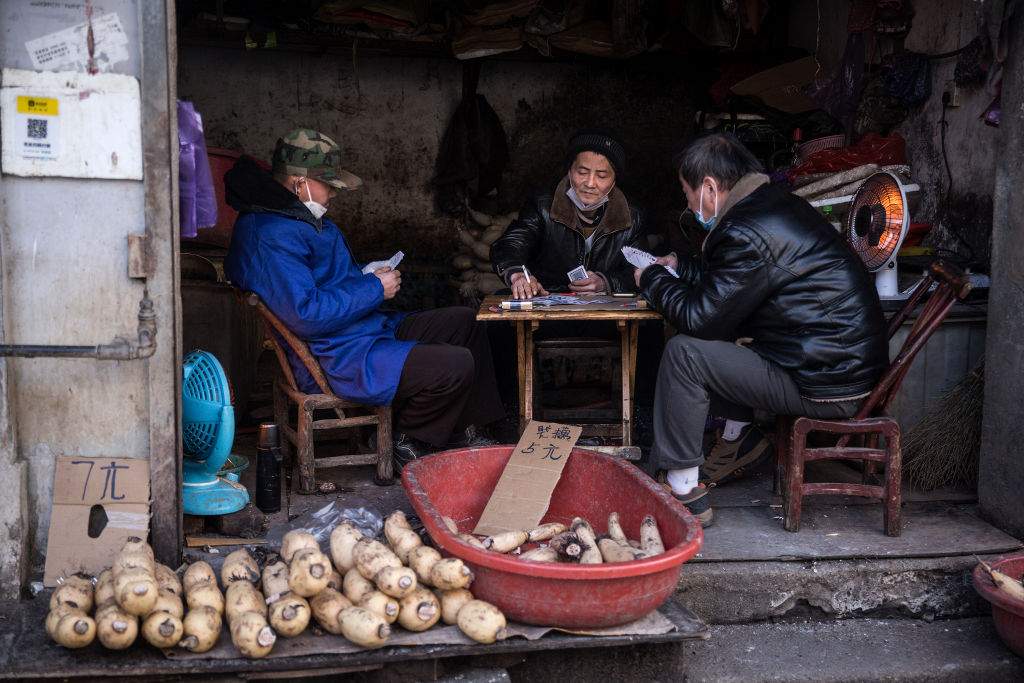 Three vendors play cards while wearing protective masks in an alley on Jan. 31, 2020 in Wuhan, China.