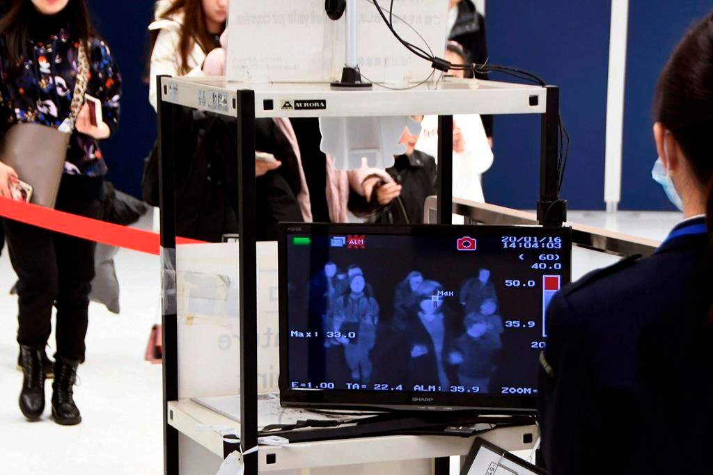 In this Jan. 16, 2020, photo, travelers from China's Wuhan go through body temperature scanners at Narita airport in Narita, near Tokyo. A fourth person has died in an outbreak of a new coronavirus in China, authorities said Tuesday, Jan. 21, 2020, as more places stepped up medical screening of travelers from the country as it enters its busiest travel period. (Kyodo News via AP).