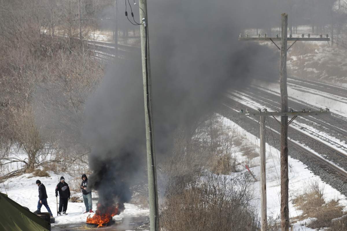 People stand next to a pile of tires on fire near to a second smaller encampment during a raid to the Tyendinaga Mohawk Territory main camp in Tyendinaga, Ontario, Canada February 24, 2020.