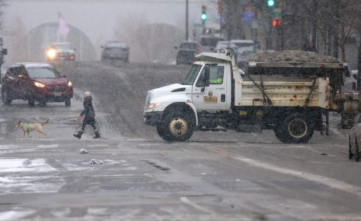 A pedestrian and a sand truck cross Boston Ave. at Sixth street in Tulsa, Okla., on Feb. 5, 2020. A winter storm blanketed the region in snow.