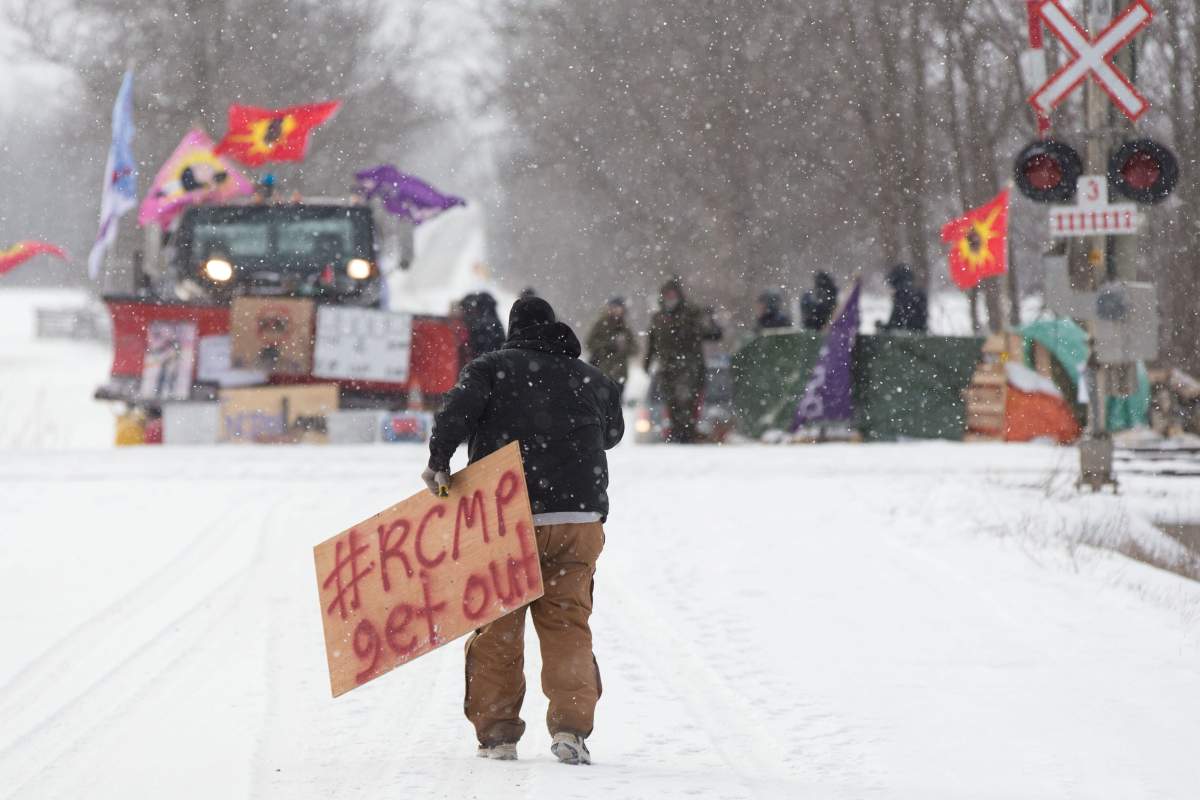 A protester carries a sign at a rail blockade on the tenth day of demonstration in Tyendinaga, near Belleville, Ont., Feb. 15, 2020.