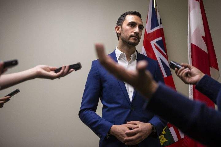 Ontario Education Minister Stephen Lecce talks to reporters in a PC caucus office as protesters join a demonstration organized by the teachers unions outside the Ontario Legislature, in Toronto on Feb. 21, 2020.