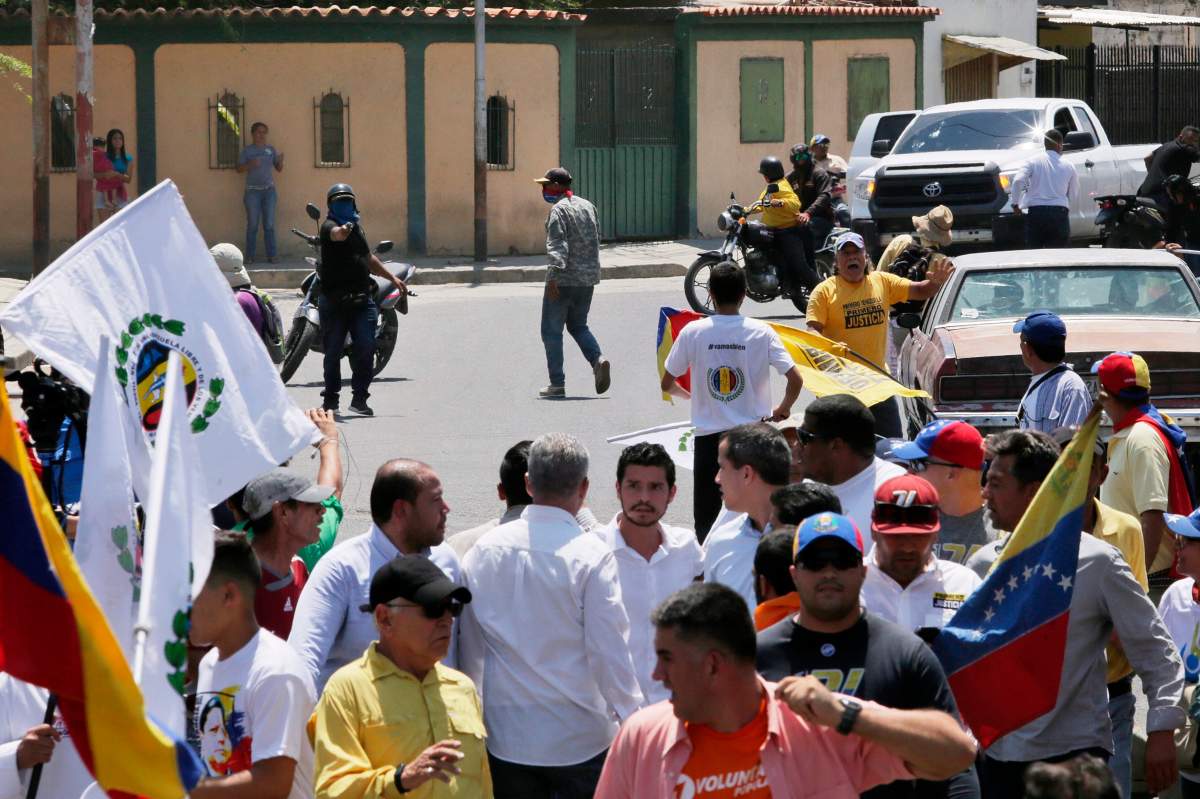 In this photo released by the Juan Guaido’s Press Office, an unidentified man aims a gun at a crowd as opposition leader Juan Guaido, centre right in light blue shirt, meets with supporters during a rally in Barquisimeto, Venezuela, Feb. 29, 2020.