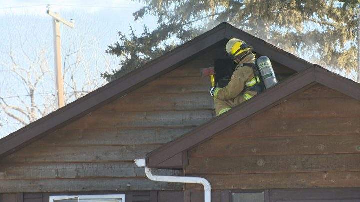 A firefighter uses an axe to get to the attic of the home on Athol Street where flames had travelled to.