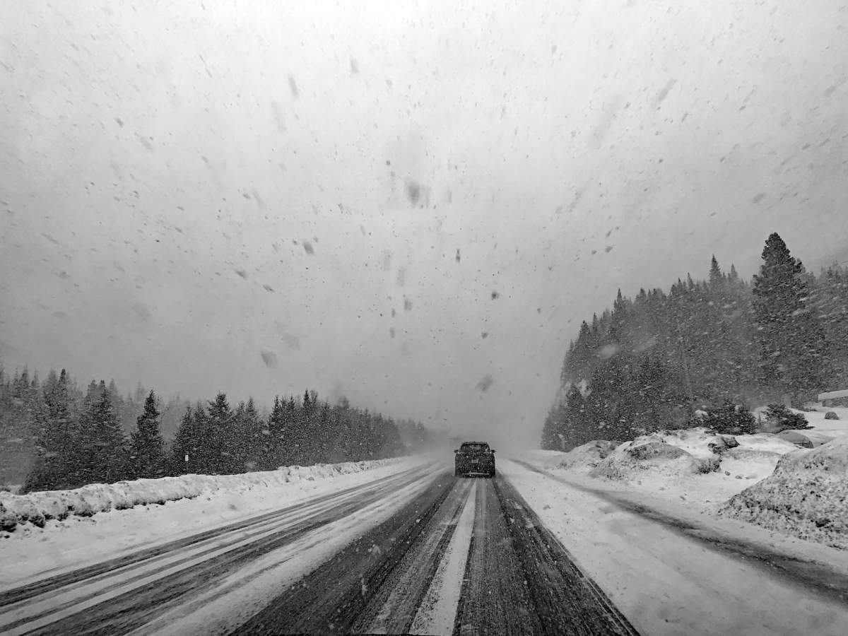 A car drives on a snowy road during a snowstorm. On each side of the road, there is a pine forest.
Photograph taken during winter 2019, near Montremblant, Quebec, Canada.