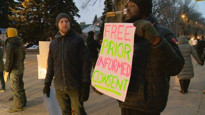 A protester holds up a sign at the Feb. 15 rally that reads “Free Prior Informed Consent”