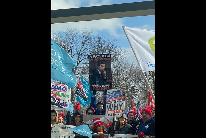 A photo of a protester outside of the Ontario PC convention on Saturday holding a sign with a photo of MPP Sam Oosterhoff and the line, "A problem an abortion could have solved.".