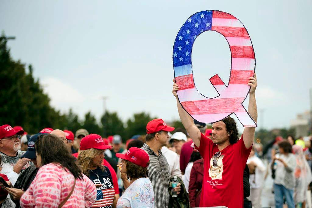 FILE - In this Aug. 2, 2018, file photo, David Reinert holding a Q sign waits in line with others to enter a campaign rally with President Donald Trump in Wilkes-Barre, Pa. A far-right conspiracy theory forged in a dark corner of the internet is creeping into the mainstream political arena. It's called QAnon, and it centers on the baseless belief that President Donald Trump is waging a secret campaign against enemies in the “deep state.”.