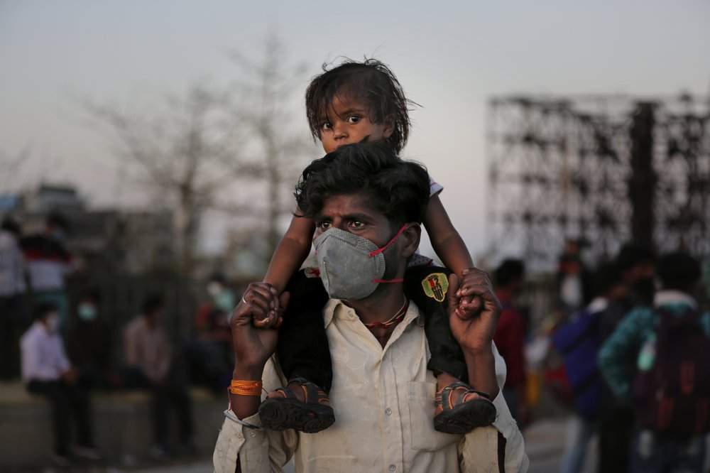 An Indian migrant worker carries a child on his shoulders as they wait for transportation to their village following a lockdown amid concern over spread of coronavirus in New Delhi, India, Saturday, March 28, 2020. Authorities sent a fleet of buses to the outskirts of India's capital on Saturday to meet an exodus of migrant workers desperately trying to reach their home villages during the world's largest coronavirus lockdown. Thousands of people, mostly young male day laborers but also families, fled their New Delhi homes after Prime Minister Narendra Modi announced a 21-day lockdown that began on Wednesday and effectively put millions of Indians who live off daily earnings out of work. 
