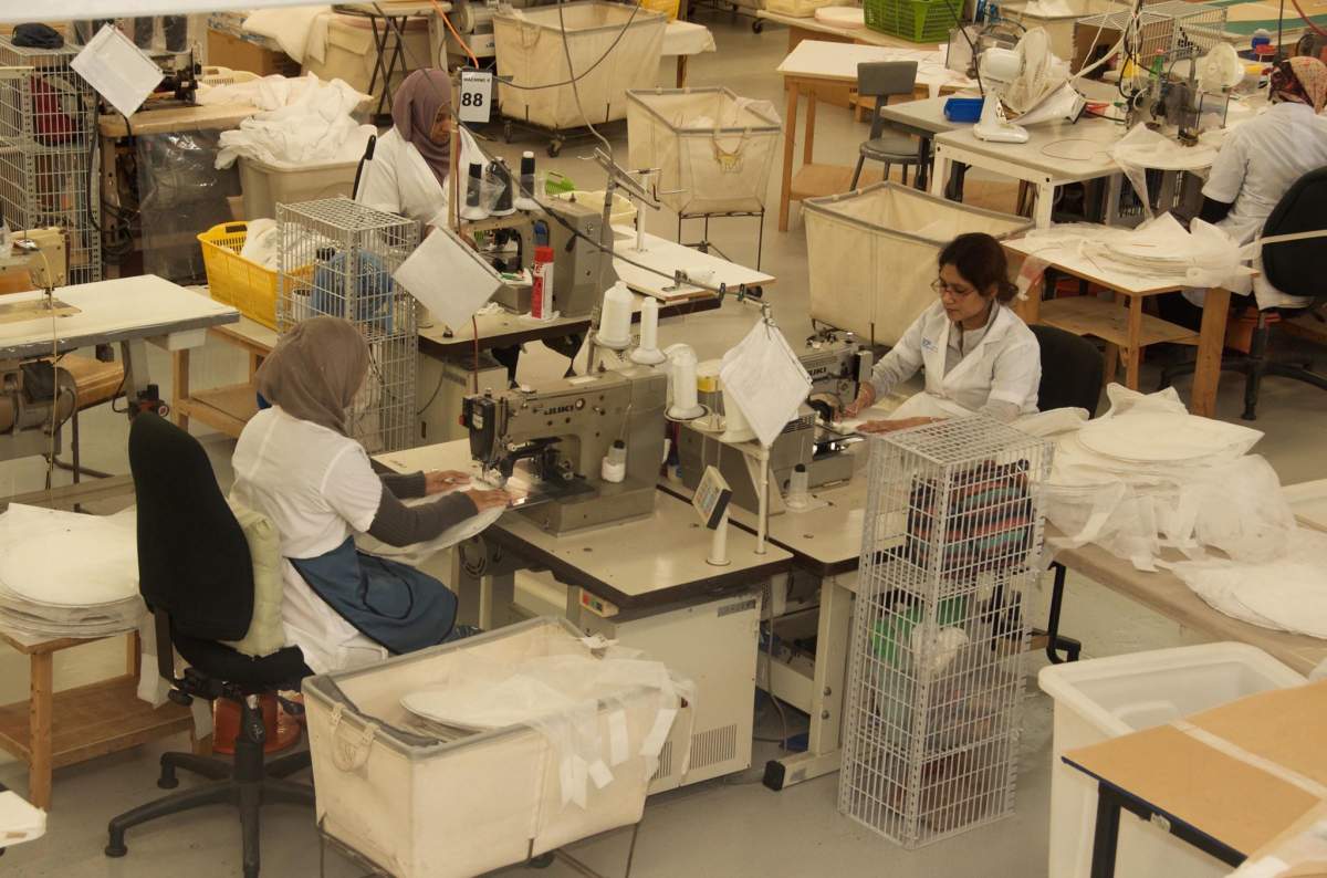 Three women who work at International Custom Products, one of the companies who have partnered with CEMM, sew personal protective equipment for Canadians front-line health care workers.