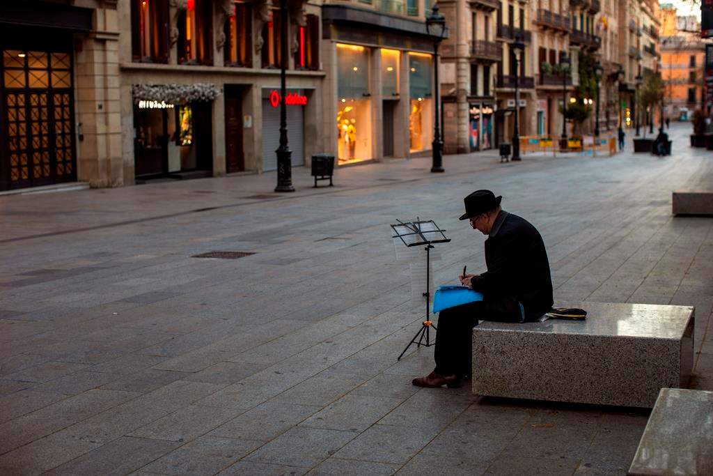 A man sits, in an empty street in Barcelona, Spain, Sunday, March 15, 2020. Spain's government announced Saturday that it is placing tight restrictions on movements and closing restaurants and other establishments in the nation of 46 million people as part of a two-week state of emergency to fight the sharp rise in coronavirus infections. For most people, the new coronavirus causes only mild or moderate symptoms. For some, it can cause more severe illness, especially in older adults and people with existing health problems.