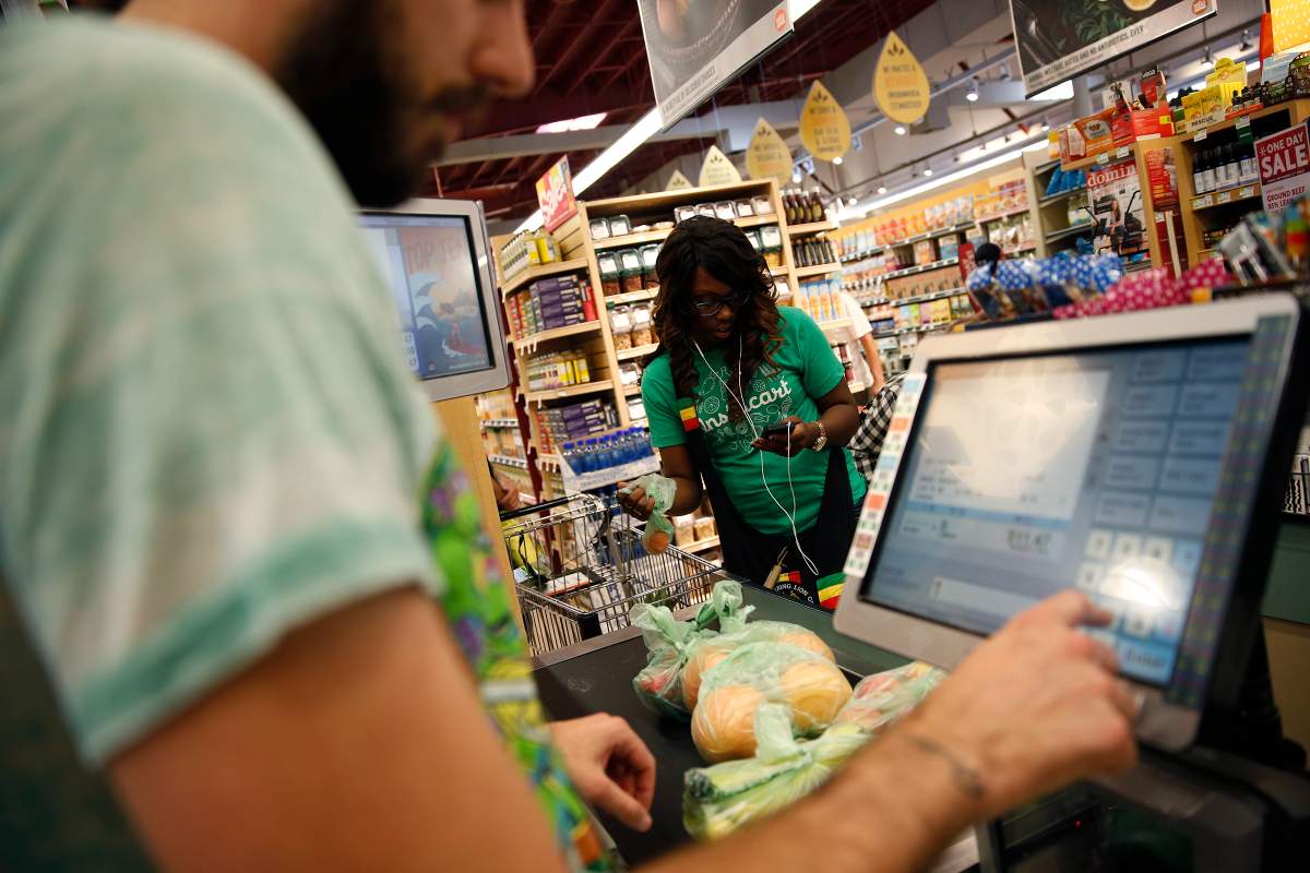 Whole Foods cashier Jason Ellsworth rings up groceries as Instacart shopper Kara Pete double checks her smartphone for items ordered by customer Tricia Carr. 