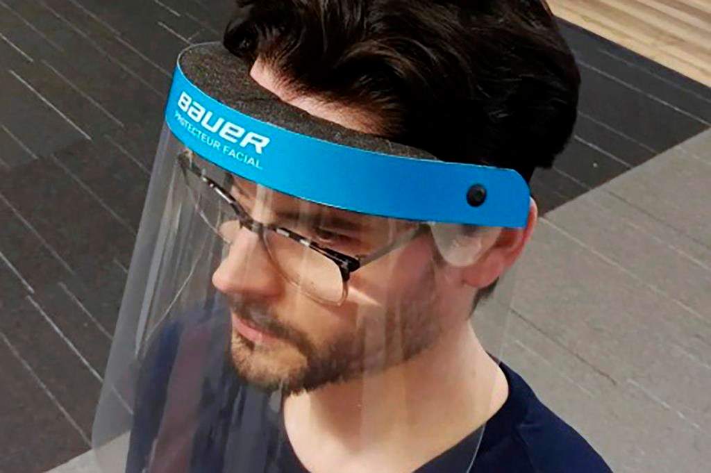 In this March 23, 2020, photo provided by Bauer Hockey Corp., an employee models a medical face shield the hockey equipment manufacturer has begun creating to help those treating the coronavirus pandemic, at Bauer Hockey Corp. in Blainville, Quebec. (Bauer Hockey Corp via AP)