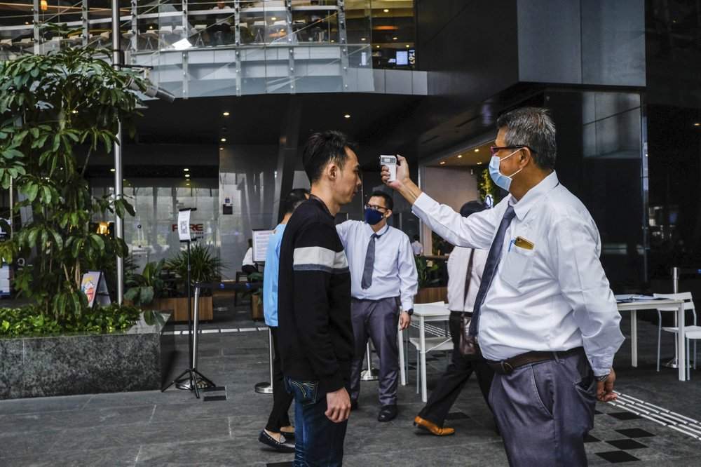 In this March 16, 2020, photo, a man scans a visitor's forehead to check his temperature before entering the Asia Square Tower in Singapore. As the virus outbreak spreads ever further, it's becoming clear that some strategies are more likely to succeed in containing it: pro-active efforts to track down and isolate cases, access to basic, affordable public health and clear, reassuring messaging from leaders. (AP Photo/Ee Ming Toh)
.