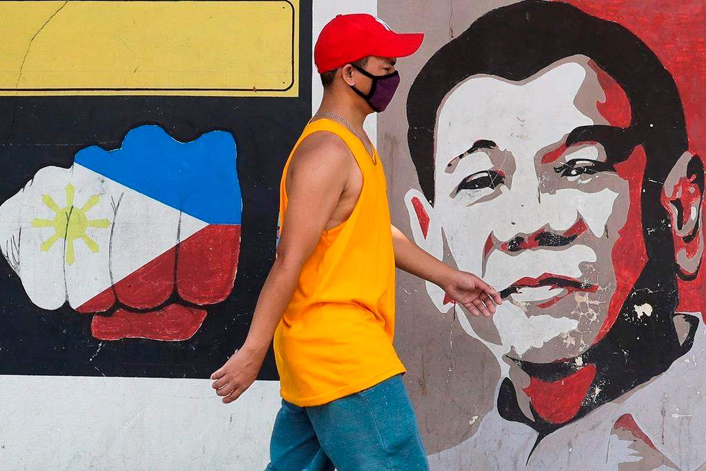 A man wearing a protective mask walks past an image of Philippine President Rodrigo Duterte in Manila, Philippines on Friday March 20, 2020.