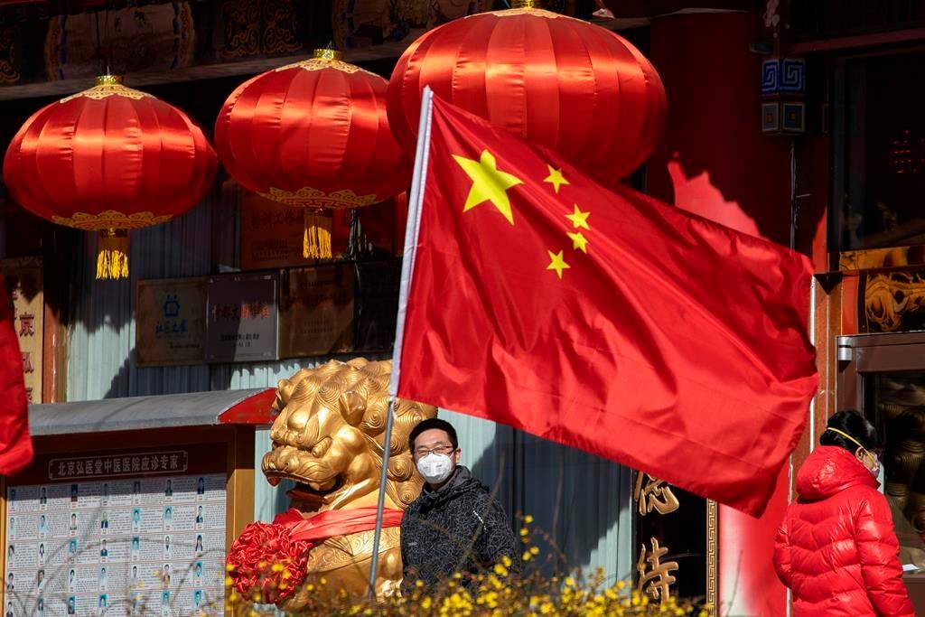 A masked man looks out near a national flag outside a traditional medicine hospital in Beijing on Tuesday, March 3, 2020.