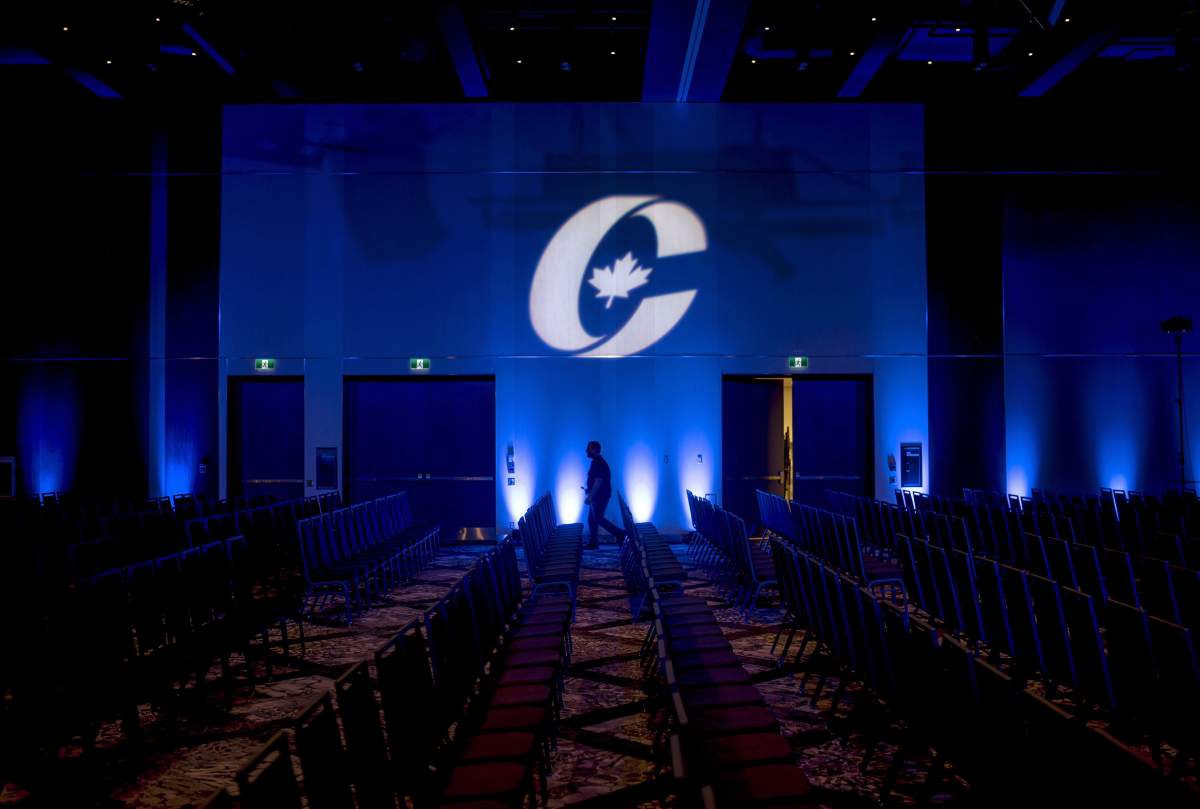 A man is silhouetted walking past a Conservative Party logo before the opening of the party's national convention in Halifax on Aug. 23, 2018.