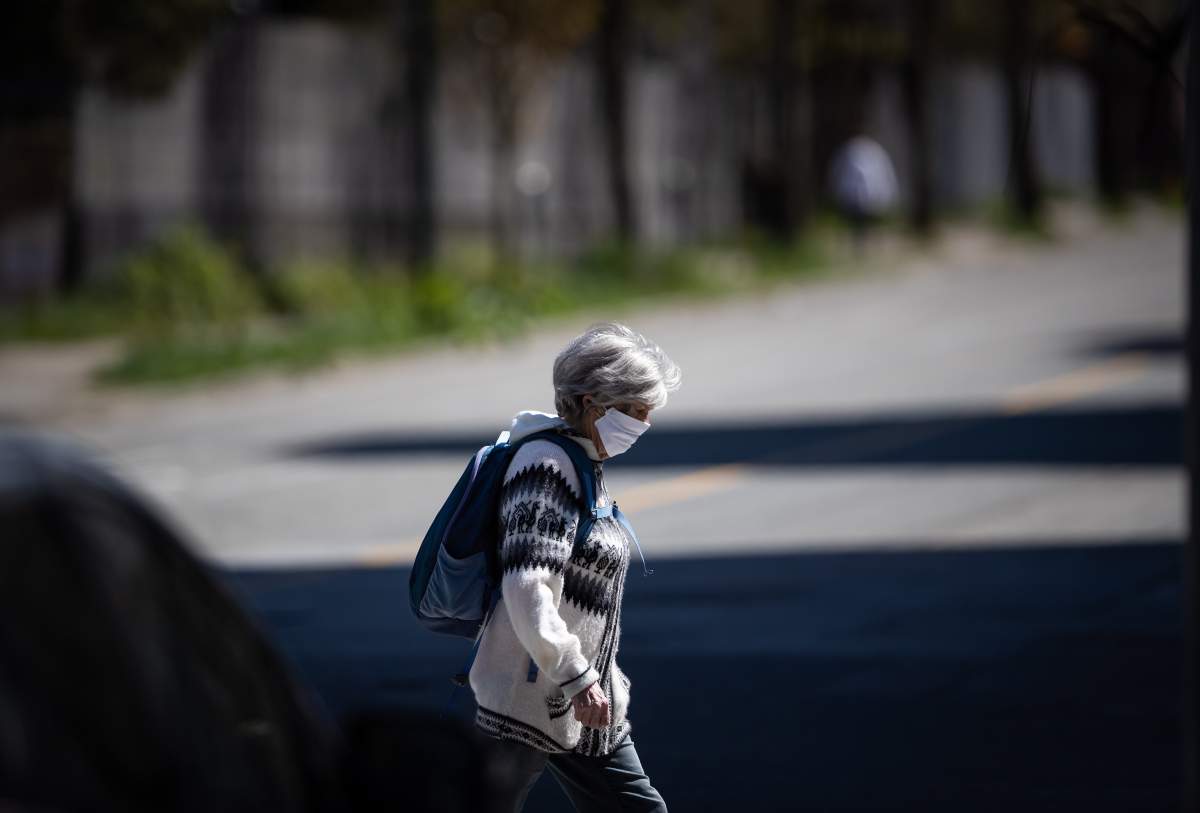 FILE - A woman wearing a fabric mask on her face walks in downtown Vancouver, on Thursday, April 16, 2020.