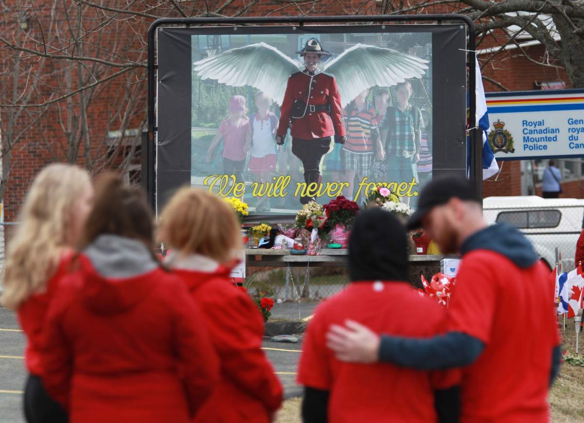 Mourners, asked to wear red on Friday, are seen near a mural dedicated to slain RCMP Const. Heidi Stevenson, during a province-wide, two-minutes of silence for the 22 victims of last weekend's shooting rampage, in front of the RCMP detachment in Cole Harbour, N.S., Friday, April 24, 2020. THE CANADIAN PRESS/Tim Krochak.