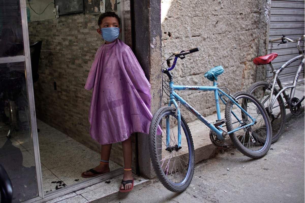 A boy wearing a protective face mask as a precaution against the COVID-19 coronavirus waits to get his haircut while standing in a doorway of a barbershop in the Mandela slum of Rio de Janeiro, Brazil, Tuesday, April 21, 2020. 
