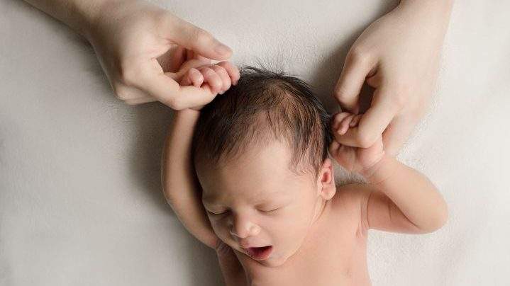 Six-day-old Callum Gudelot holds hands with his mother and father.