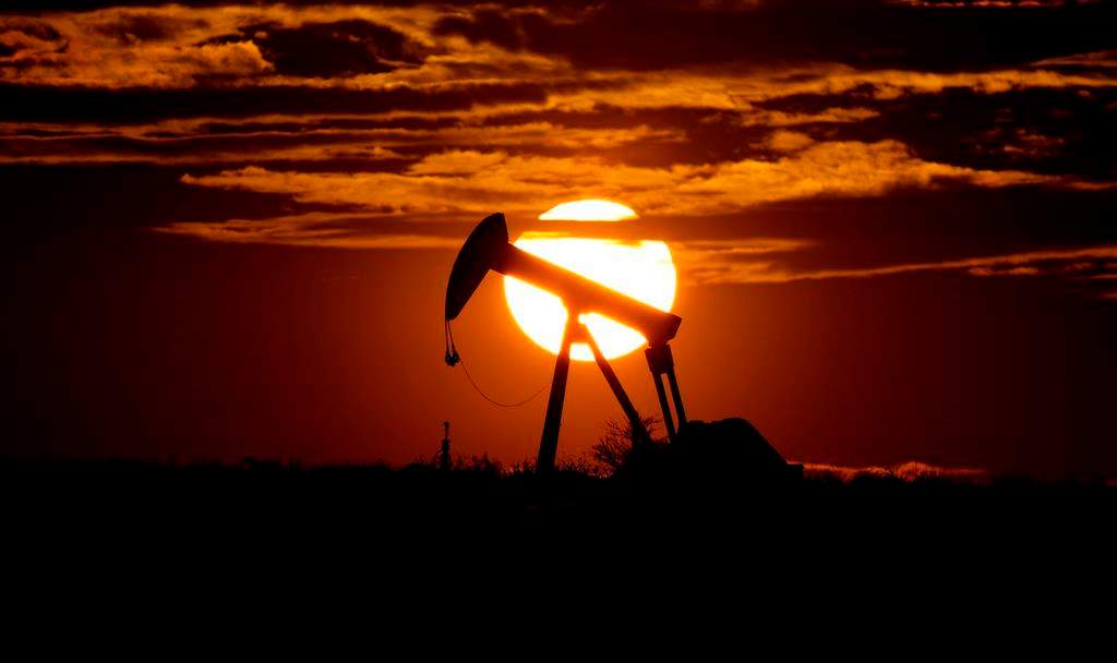 The sun sets behind an idle pump jack. 