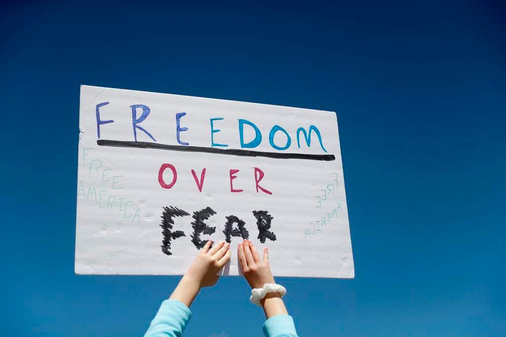 FILE - In this April 21, 2020, file photo a person holds a sign while gathering with others to protest stay-at-home orders put into place due to the COVID-19 outbreak outside the Missouri Capitol in Jefferson City, Mo. Amid pockets of attention-grabbing protests, a new survey finds Americans remain overwhelming in favor of stay-at-home orders and other efforts to slow the spread of coronavirus. (AP Photo/Jeff Roberson, File).