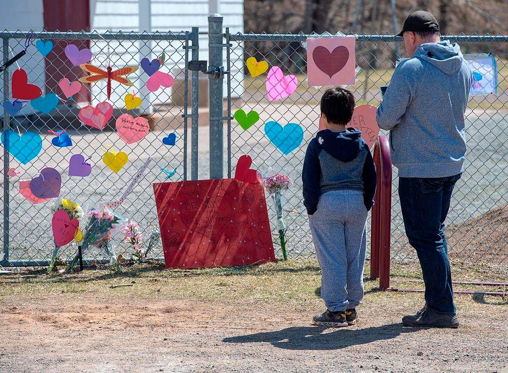 A man and his son pay repects at a memorial to Lisa McCully, a teacher at Debert Elementary School in Debert, N.S. on Tuesday, April 21, 2020.
